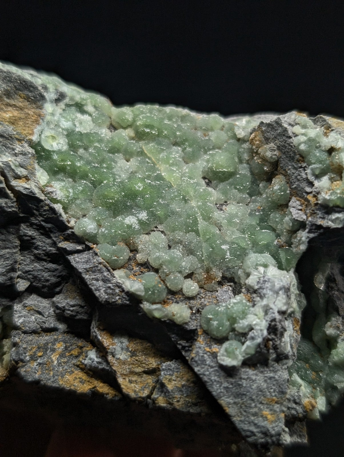 A cluster of translucent green crystals grows densely on a rugged, gray rock matrix.