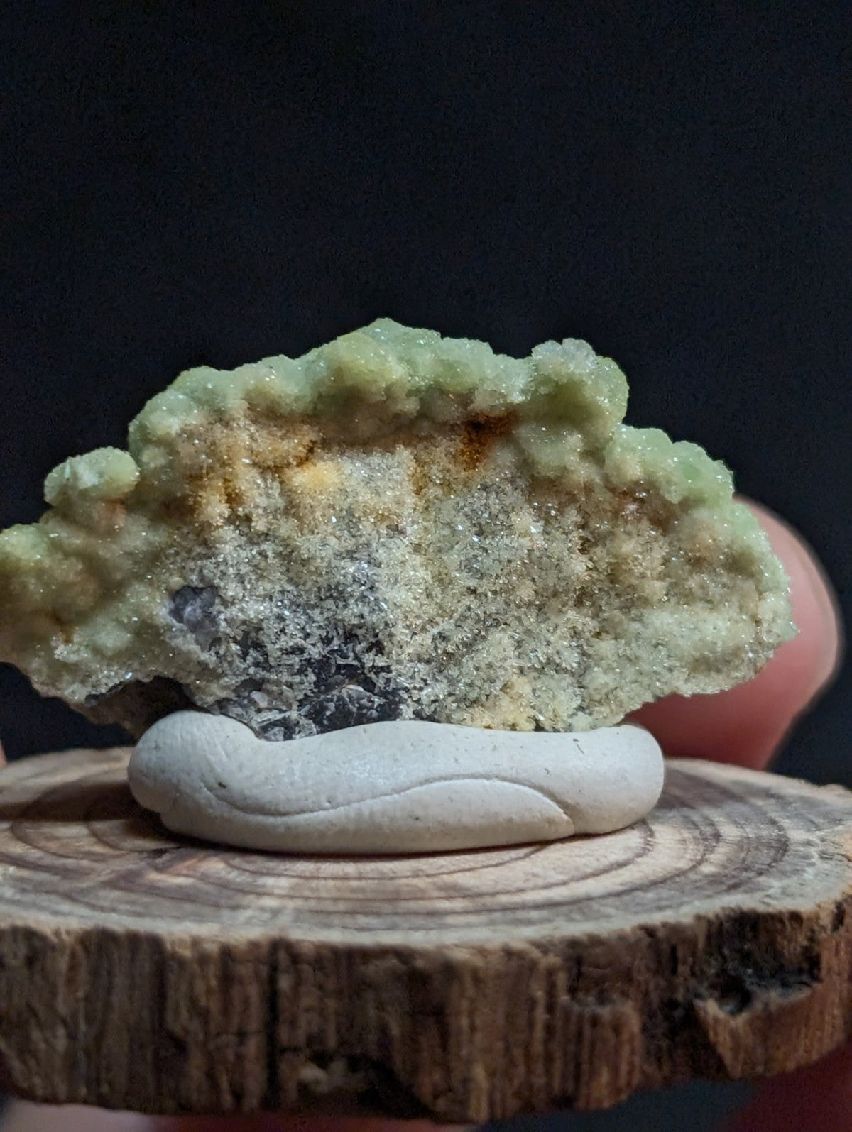 A striking green and yellow mineral specimen with a textured, crystalline surface rests on a white ceramic stand.