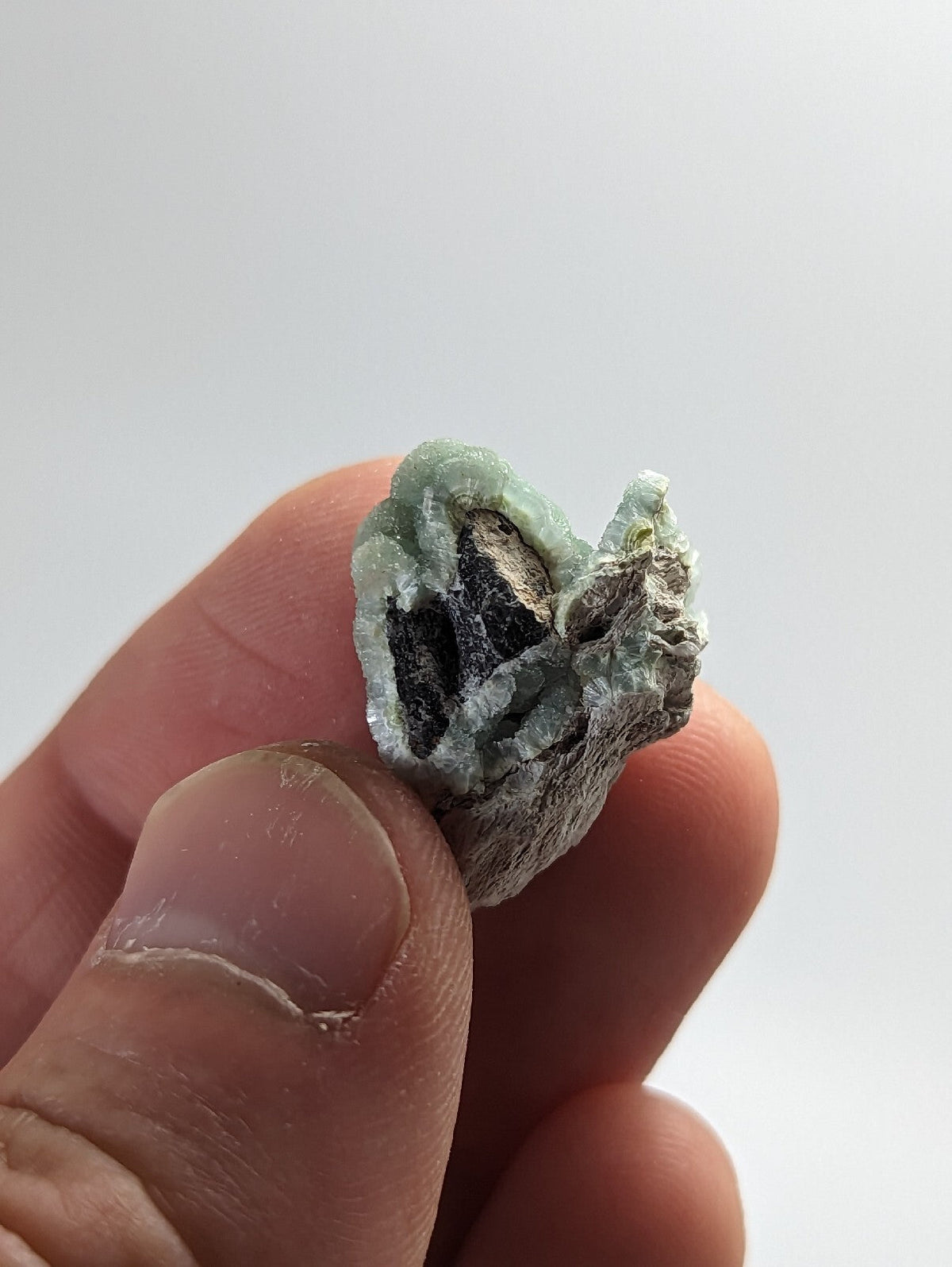 A small, irregularly shaped mineral specimen with a pale green outer crust and dark interior.