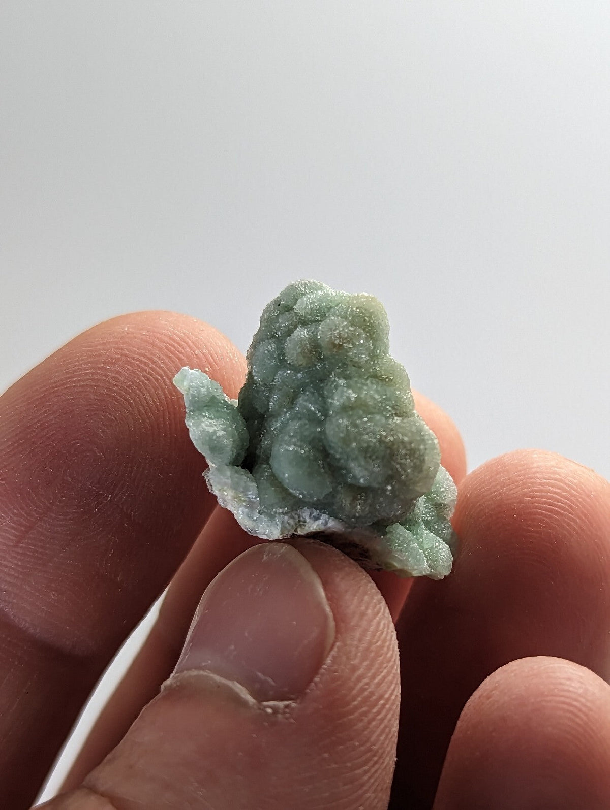 A delicate, light green mineral specimen with a textured, bumpy surface held gently between fingers.