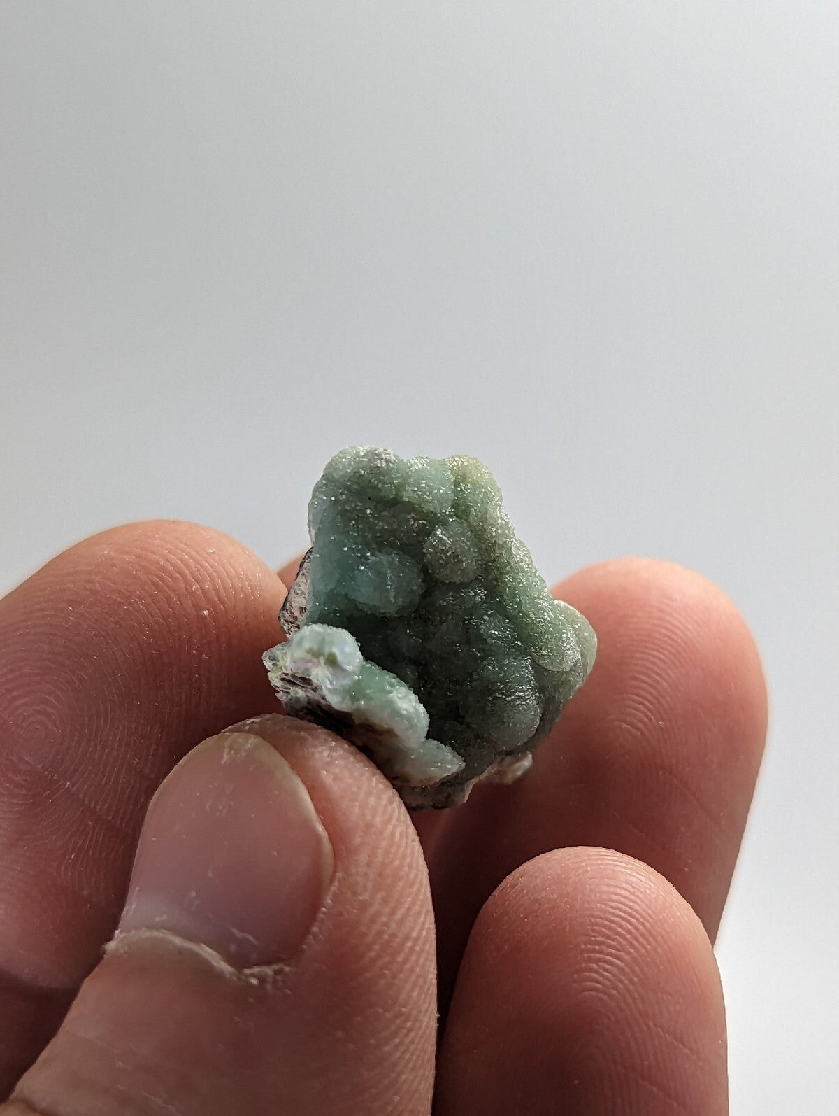 A small, textured green mineral specimen with a rough, crystalline surface and some white patches.