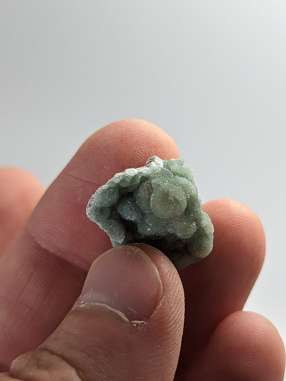 A delicate, pale green mineral specimen with a crystalline, clustered texture.