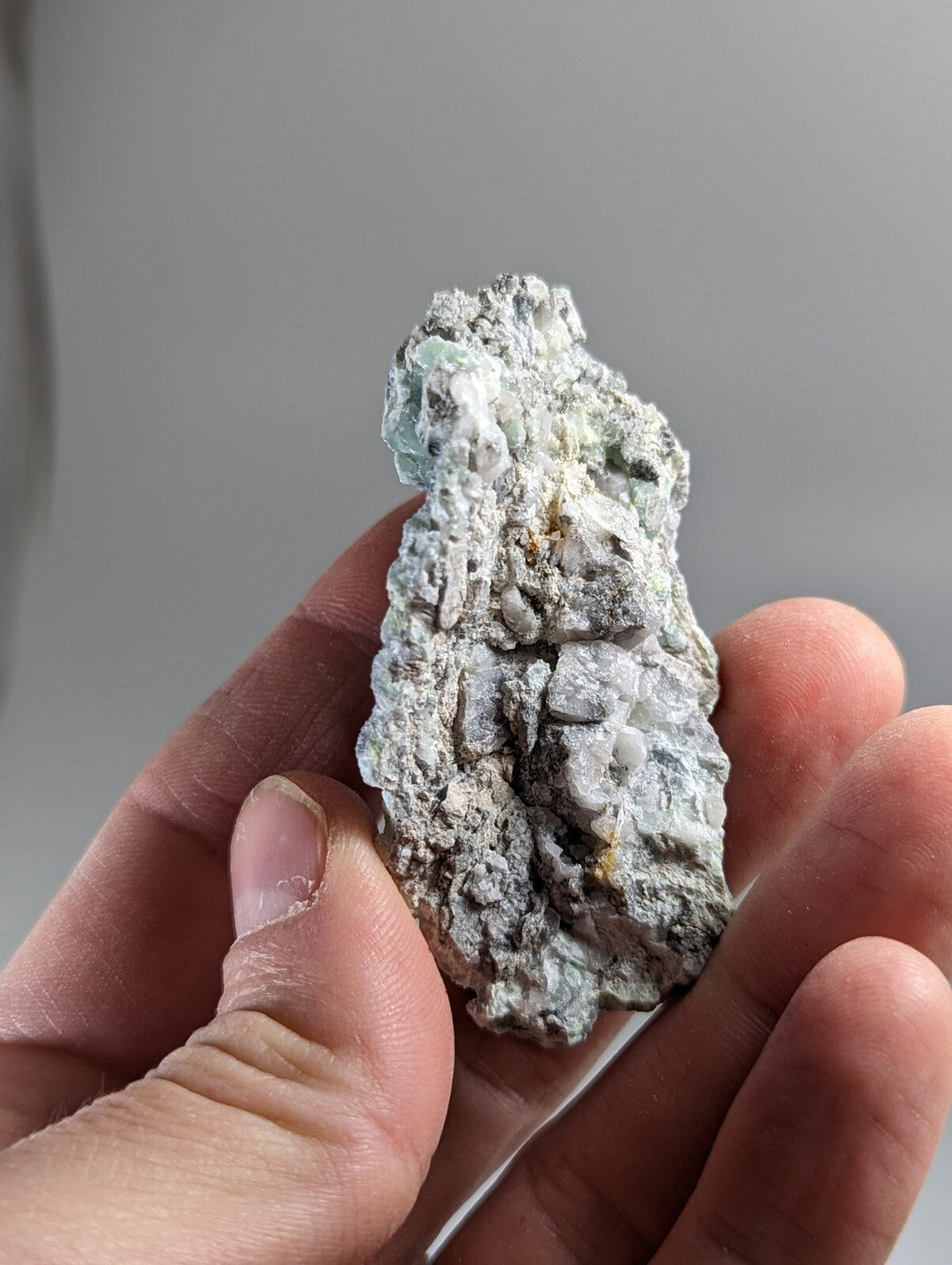 A rough, irregularly shaped mineral specimen with a mottled gray and pale green surface.