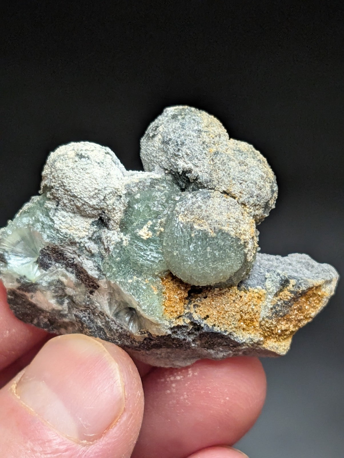 A hand holds a cluster of translucent green and gray mineral specimens with rounded, bulbous formations.