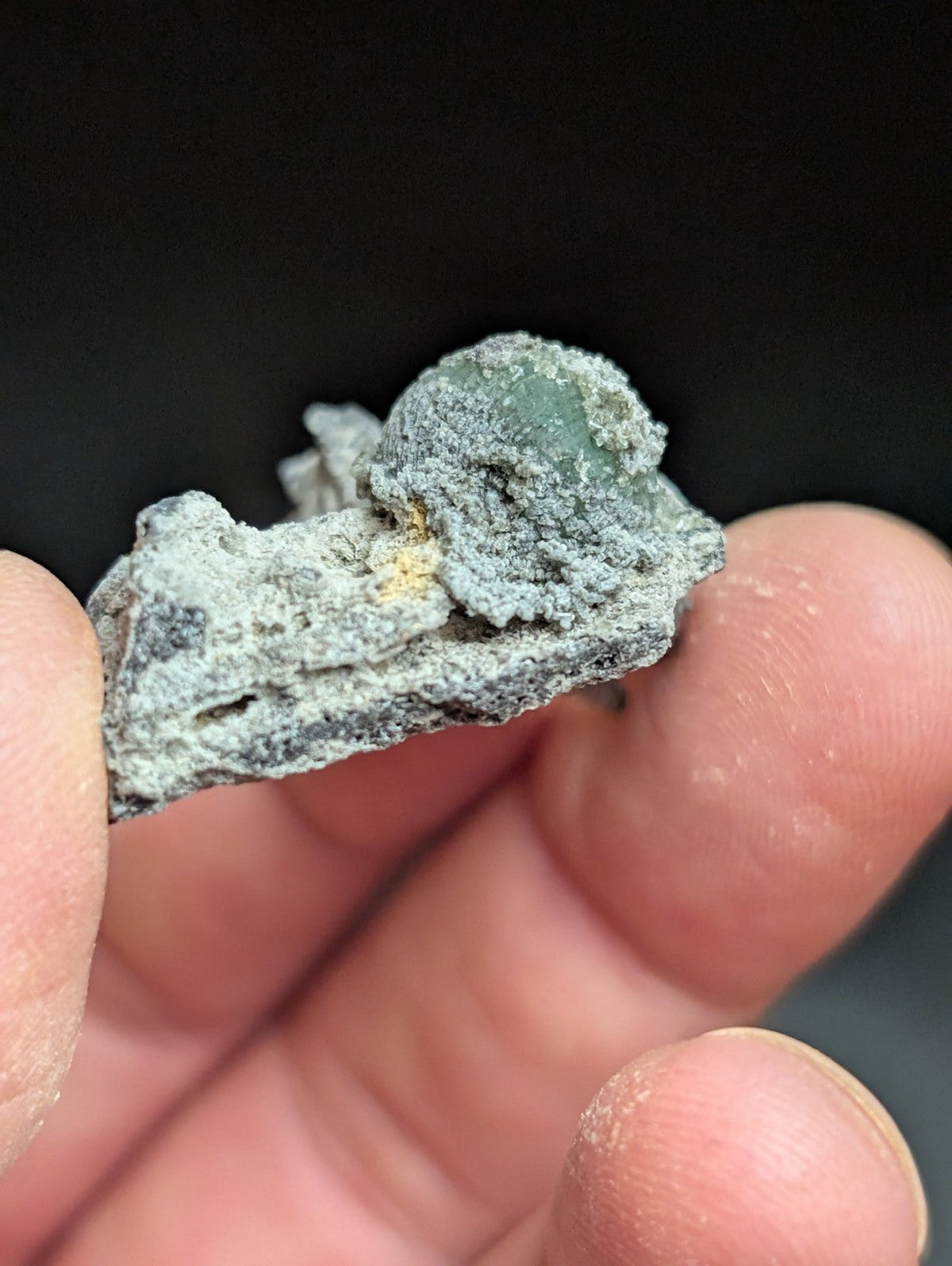 A weathered, grayish-green mineral specimen with a rough, textured surface and subtle hints of yellow.