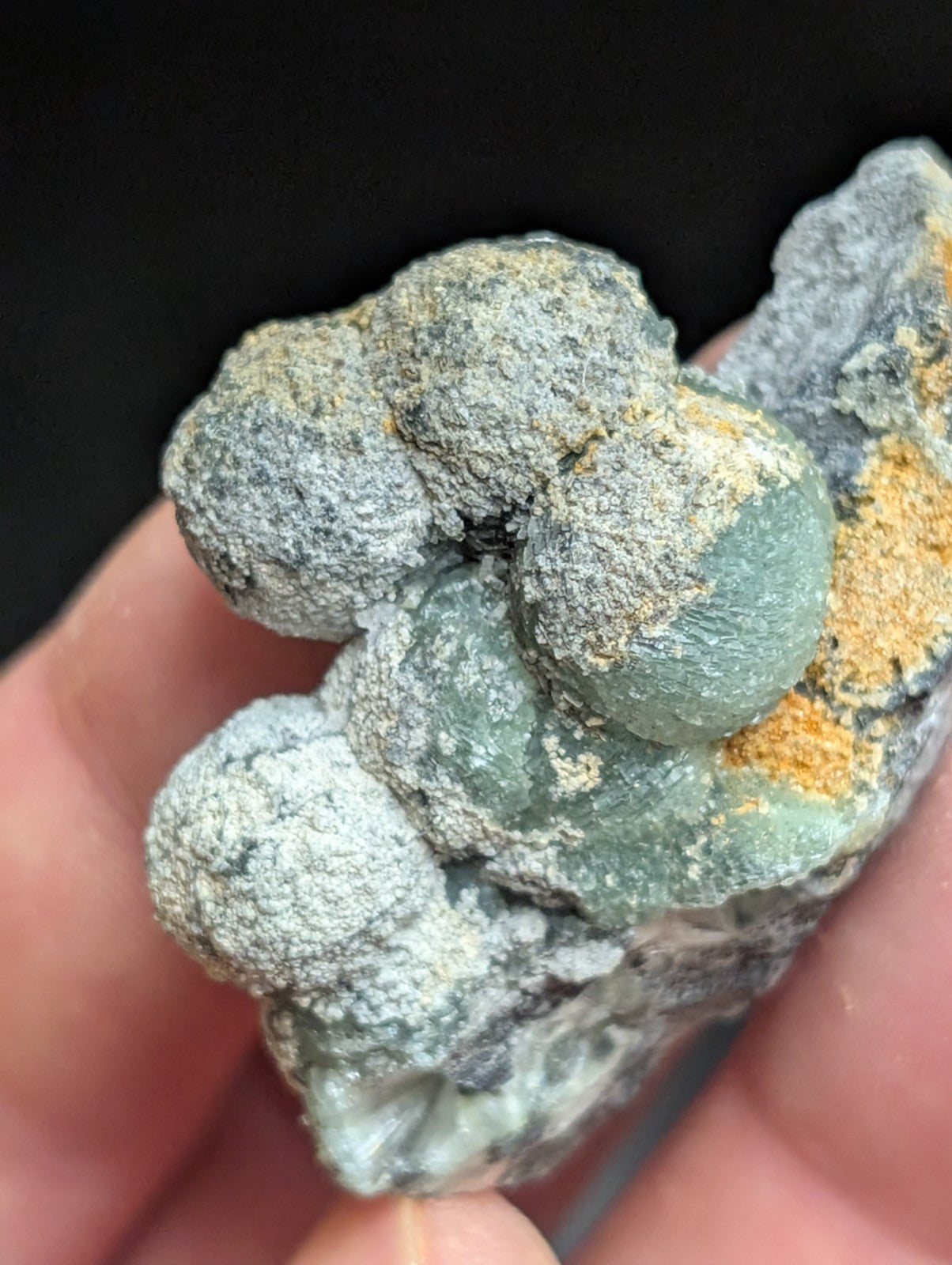 A cluster of greenish-gray, rounded mineral formations with a rough, textured surface and subtle orange-yellow patches.