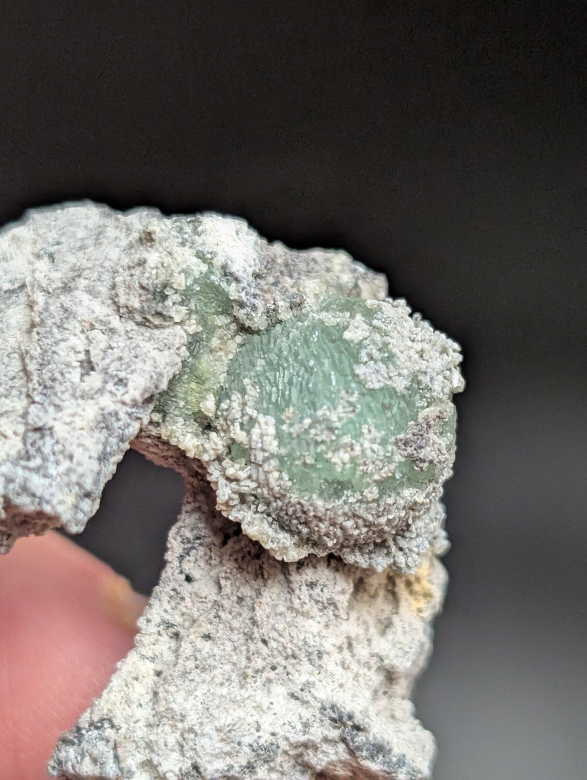 A translucent green mineral specimen embedded in a rough, white crystalline matrix.