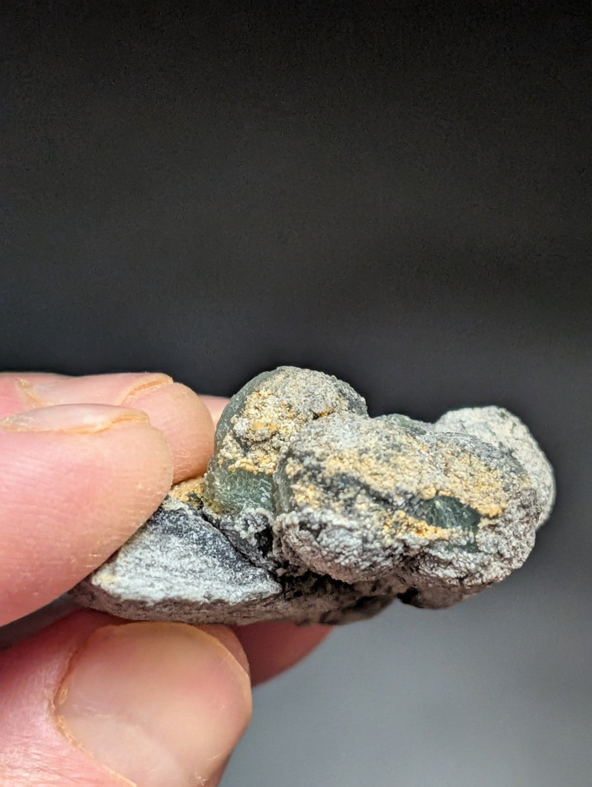 A rough, irregularly shaped mineral specimen with a grayish base color and patches of yellowish-green veining.