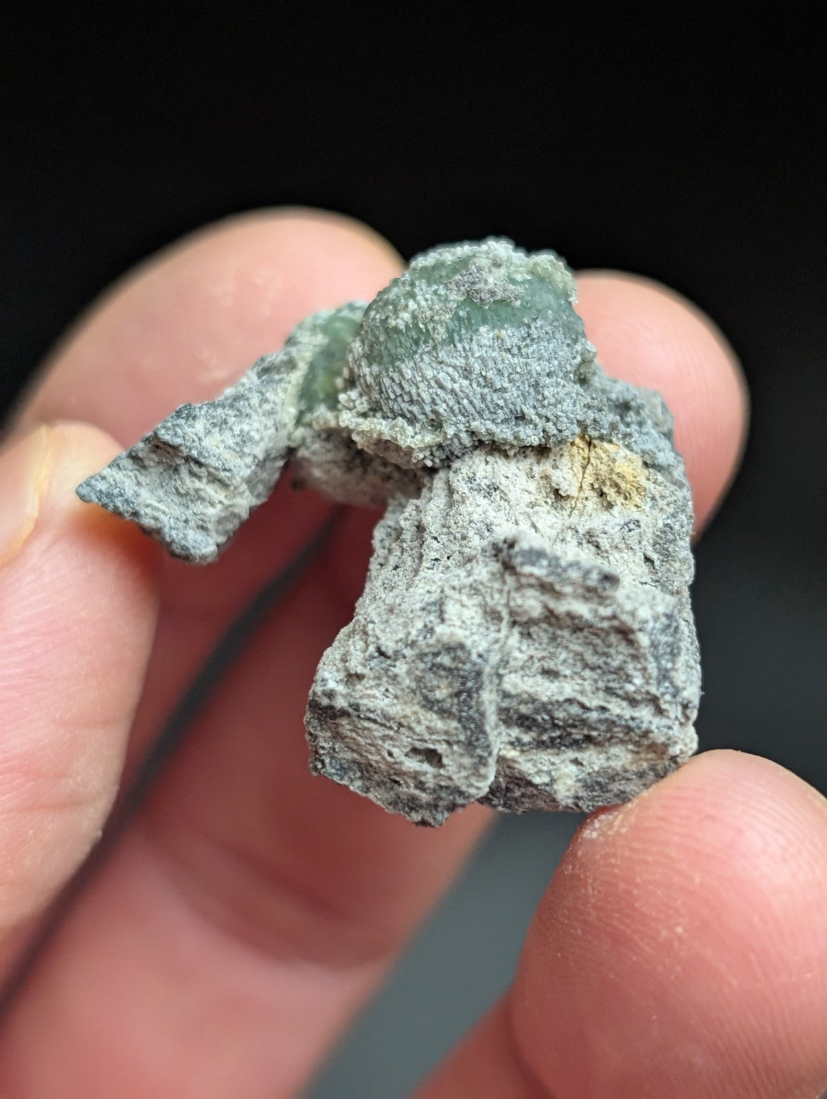 A weathered, gray-green patina-coated miniature figurine with a textured surface and faint hints of original color peeking through.
