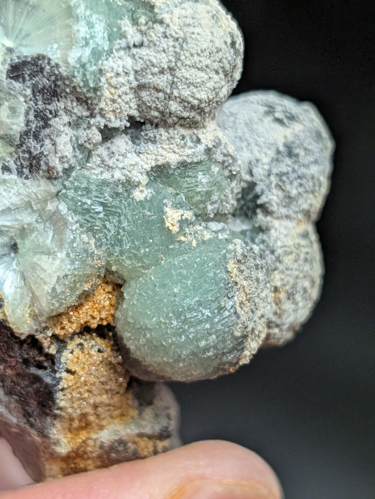 A cluster of translucent greenish-blue crystals with a rough, textured surface and white mineral coating.