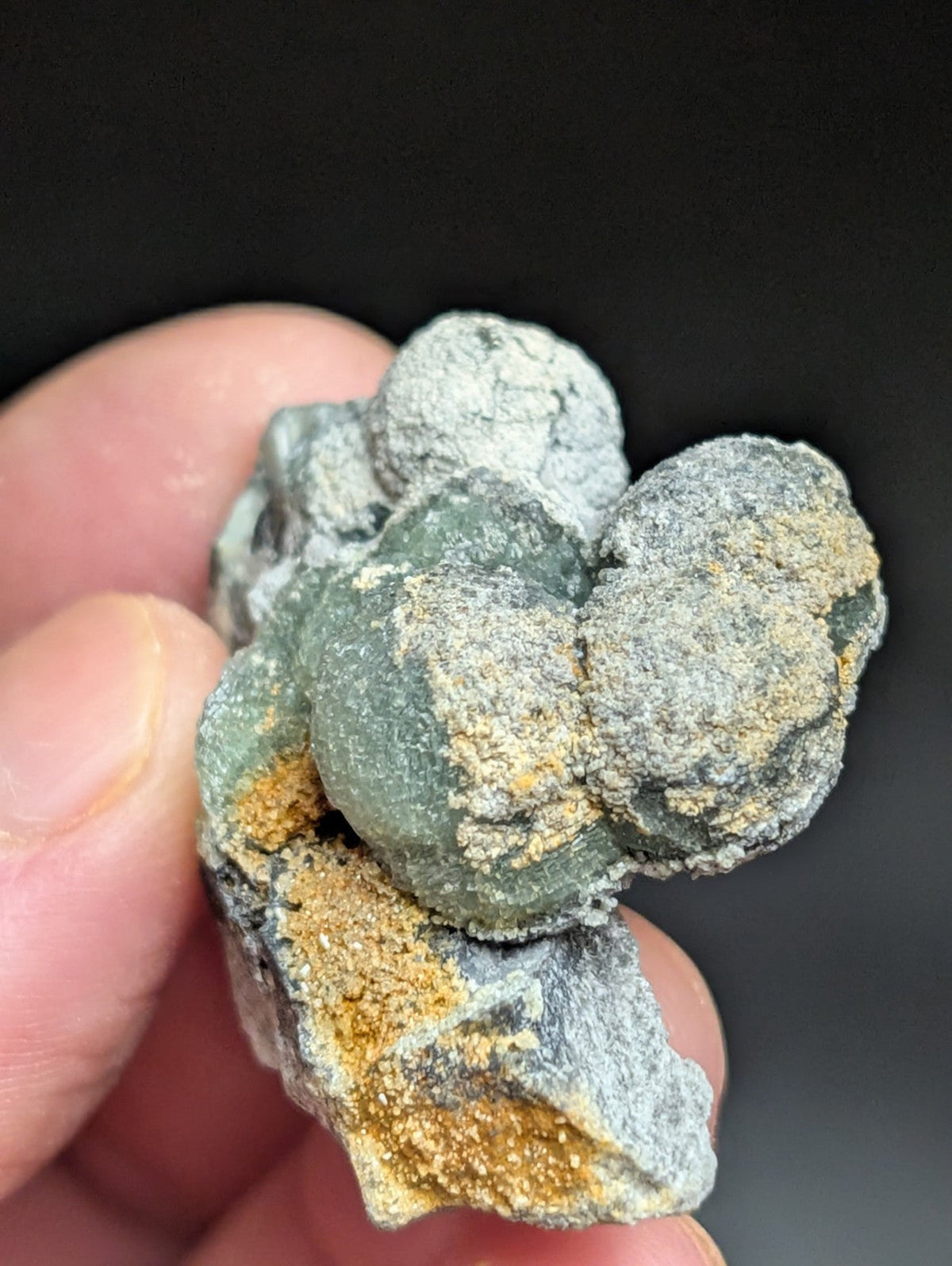 A cluster of green and gray mineral formations with patches of yellowish-orange crust.