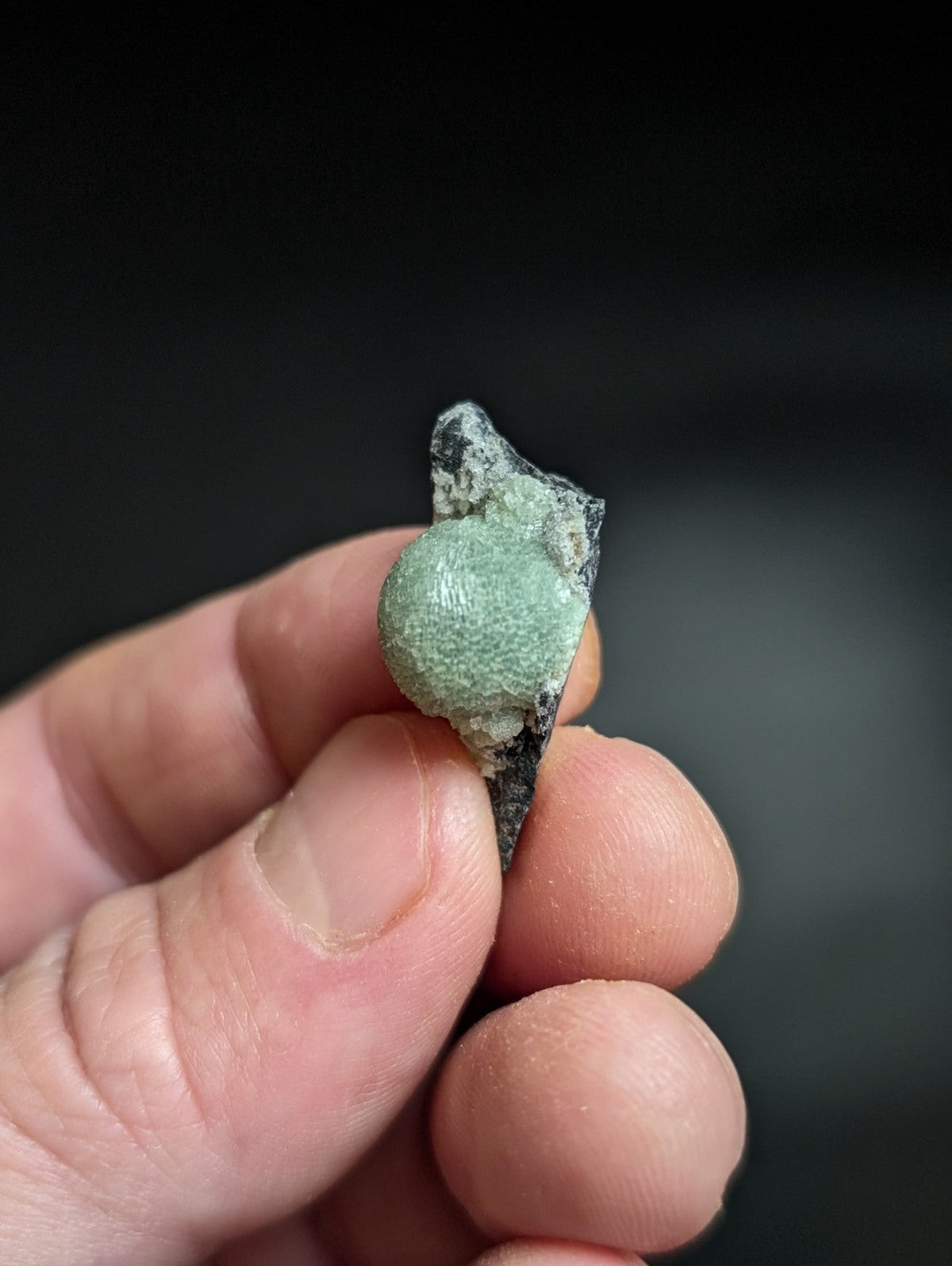 A weathered, greenish patina-coated ancient bronze artifact with a rounded bulbous section and jagged edges.