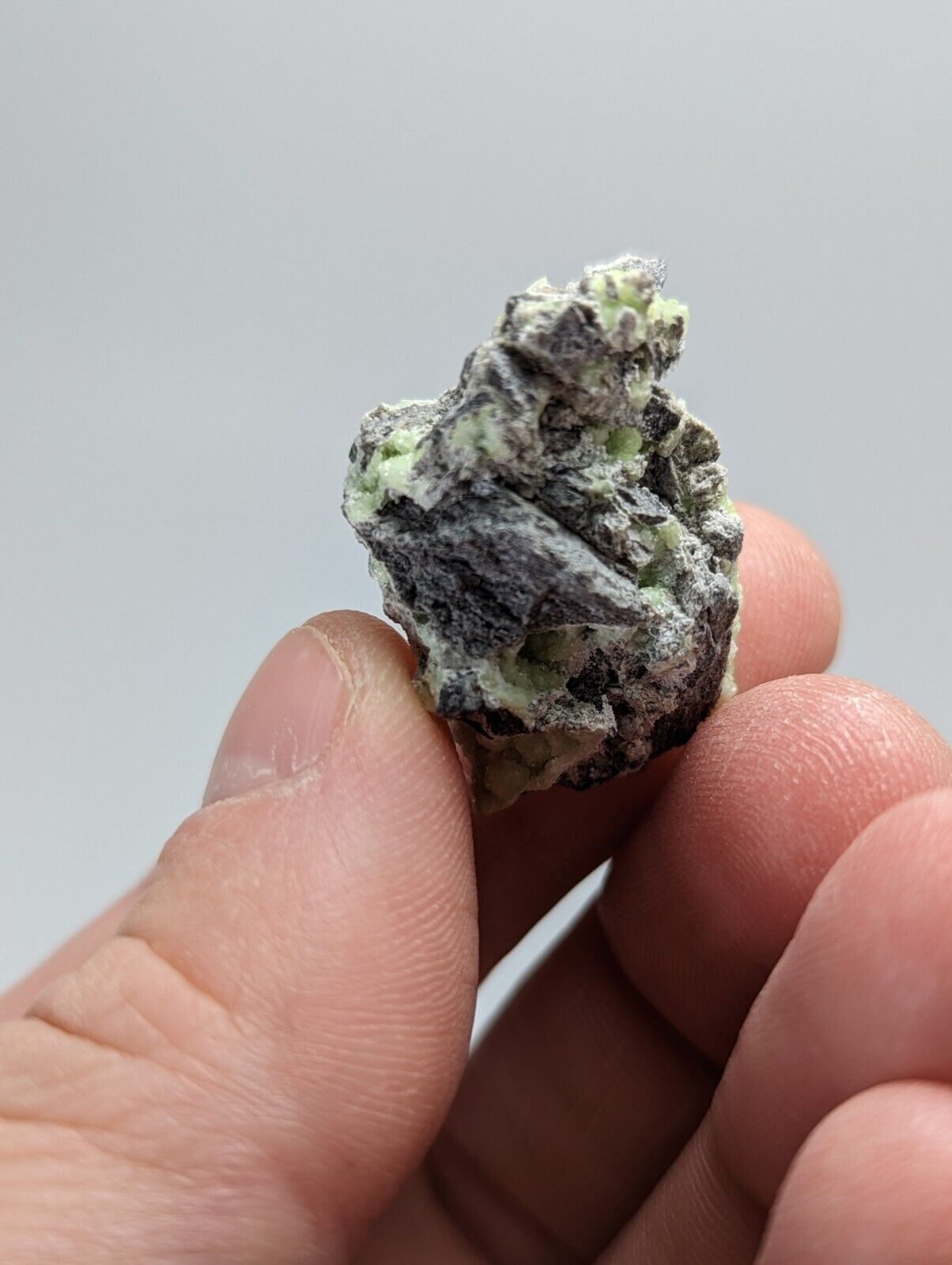 Hand-held, rough, dark and light green mineral specimen.