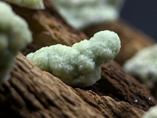 A pale green, crystalline mineral formation with a rough, textured surface rests on dark brown wood.