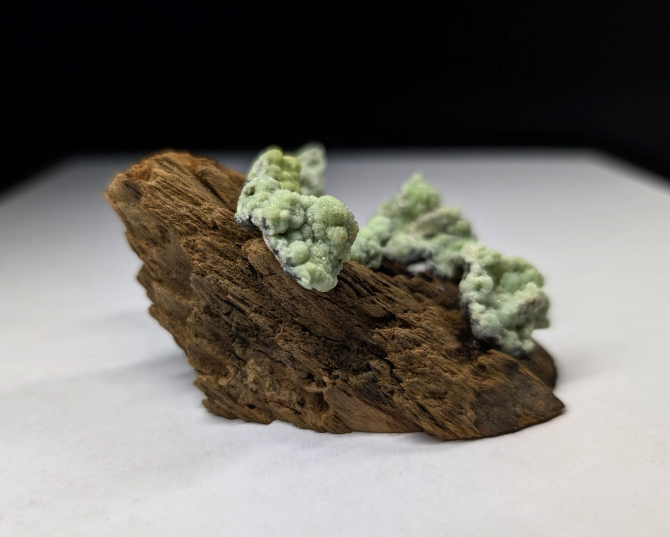 A natural mineral specimen featuring light green, clustered crystals growing atop a rugged brown rock base.