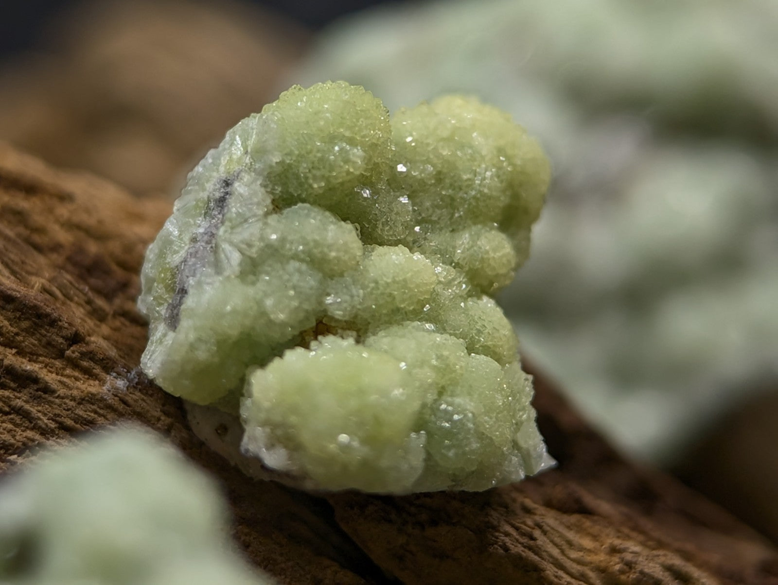 A cluster of pale green, crystalline minerals with a rough, textured surface resting on wood.