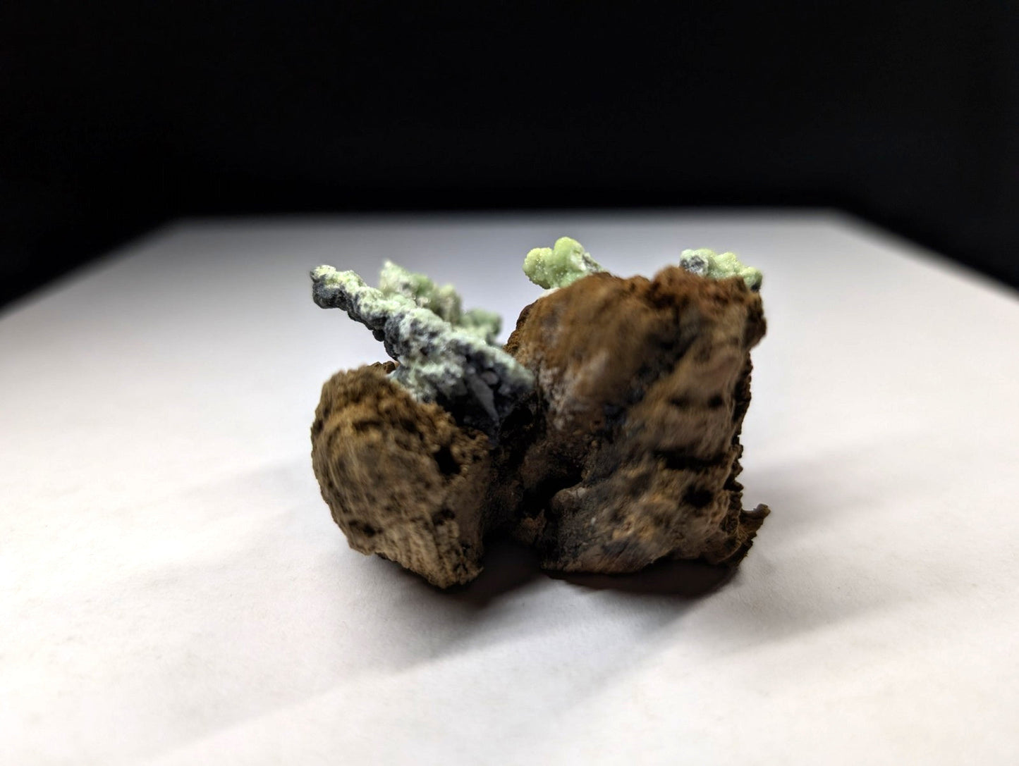 A rugged, earthy brown mineral specimen with intricate green and gray crystalline formations.