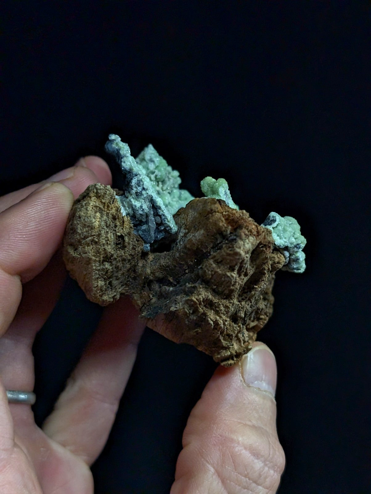 A rugged, earthy brown rock specimen with patches of vibrant green patina and hints of blue-green mineral growth.