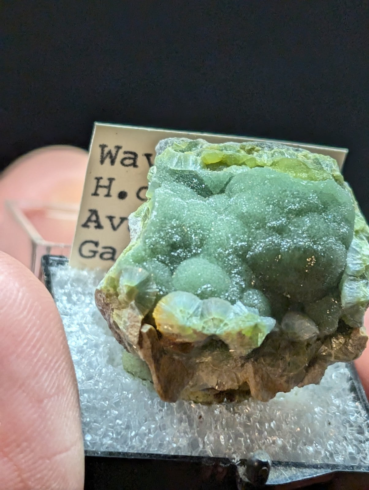 A green, translucent wavellite mineral specimen with a rough, crystalline surface and earthy brown base.