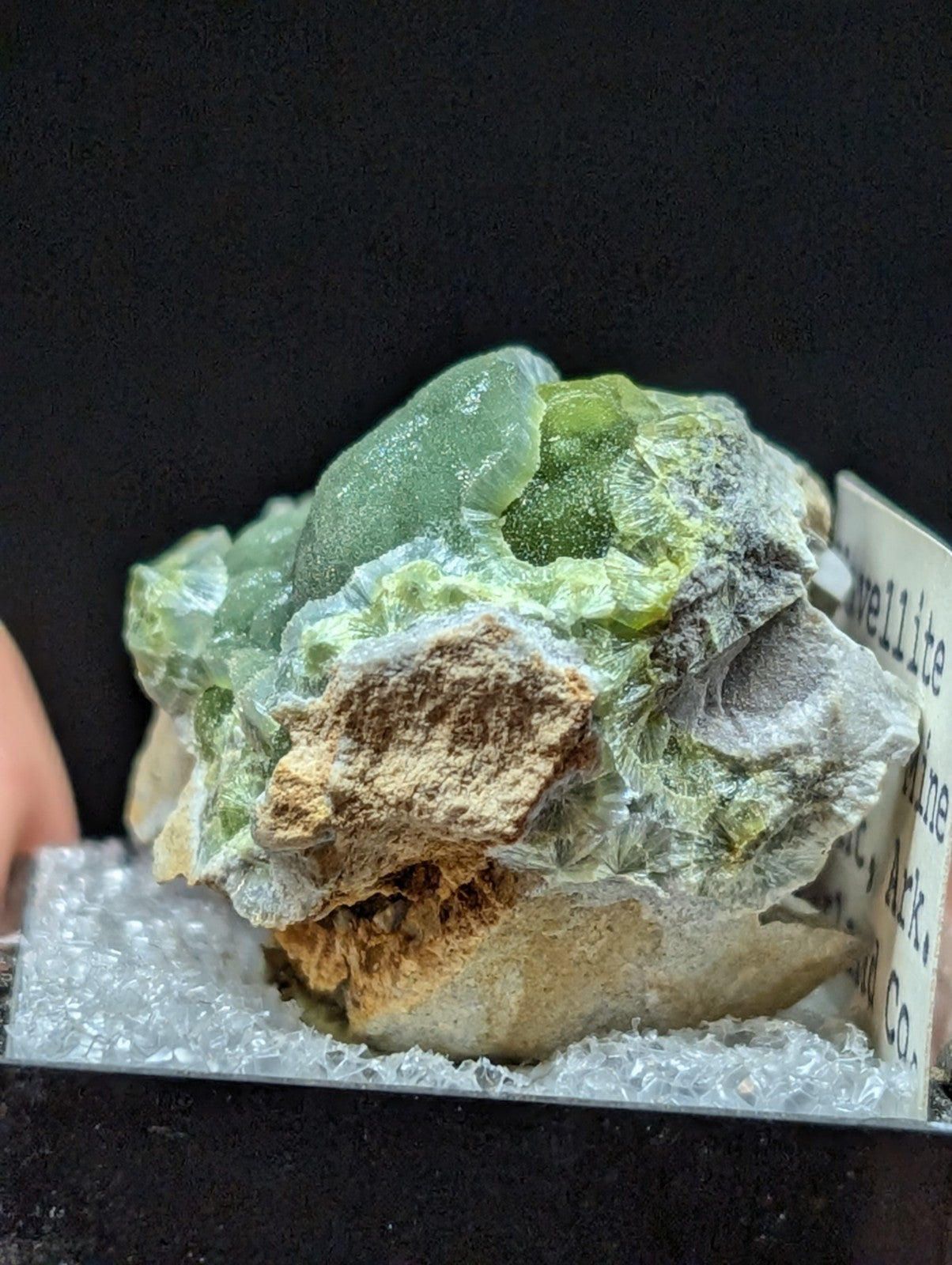 A translucent green fluorite specimen with crystalline formations nestled atop a matrix of earthy brown and gray rock.