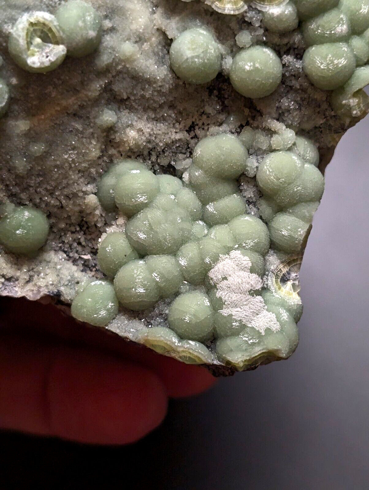 A cluster of translucent, pale green spherical crystals growing from a rough, grayish rock matrix.