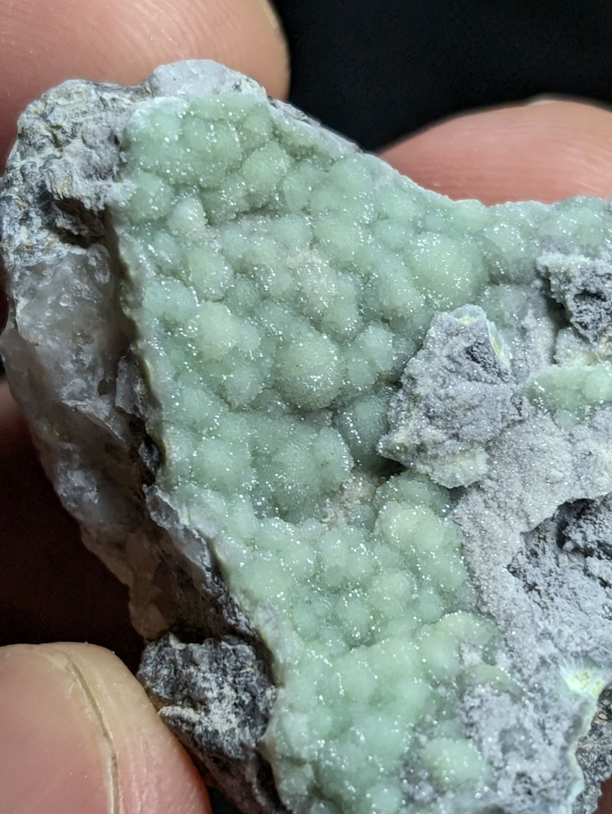 A pale green, crystalline mineral formation with a textured, bubbly surface embedded in gray rock.