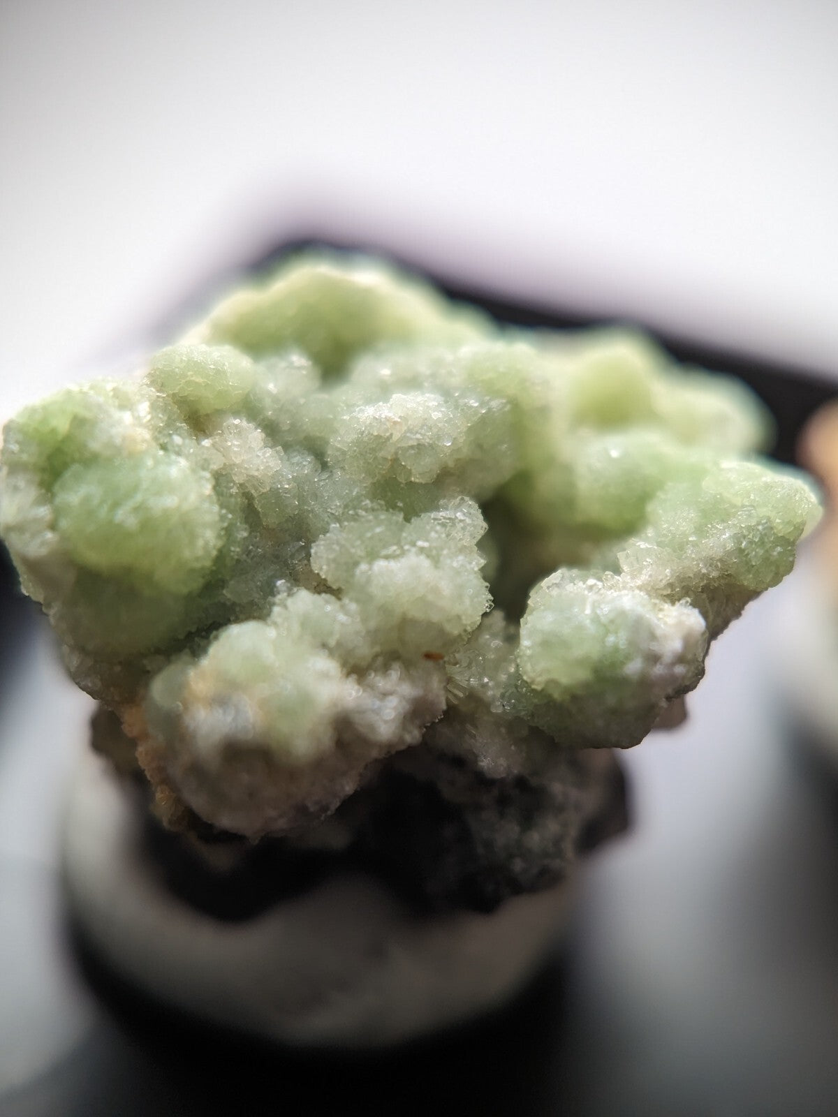 A pale green, crystalline mineral specimen with a textured, clustered surface.