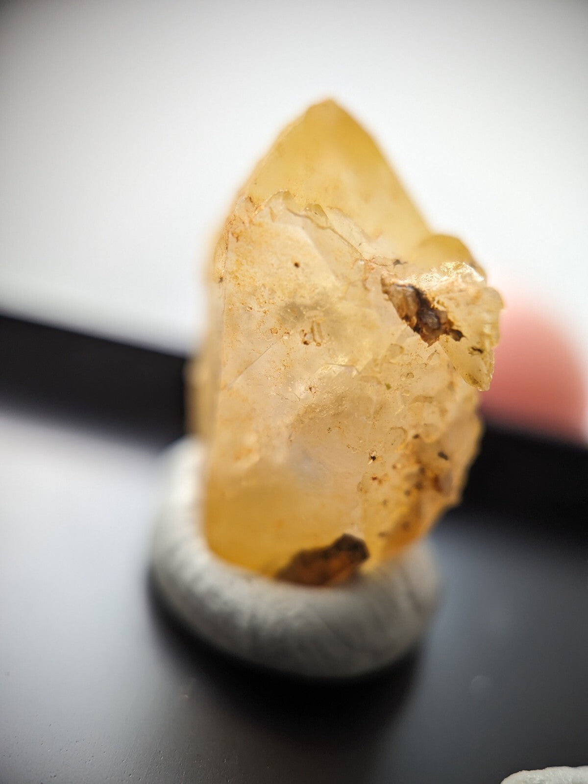 A translucent golden-yellow citrine crystal with natural inclusions, displayed on a textured white pedestal.