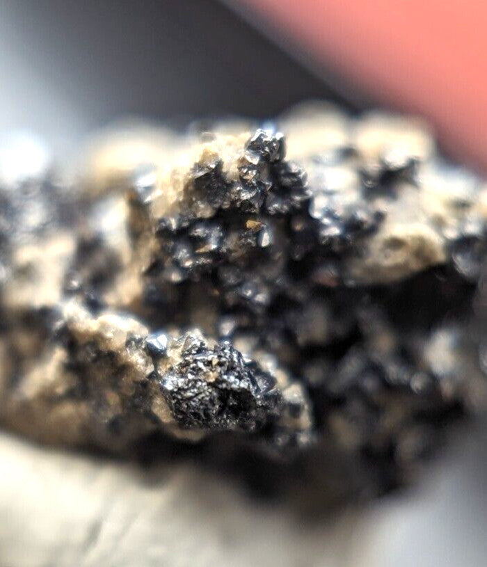 A rough, irregularly shaped mineral specimen with a dark black and metallic sheen interspersed with lighter beige patches.