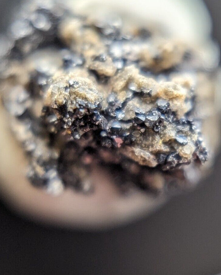 A close-up of a textured, crumbly substance with dark black and light beige speckles.