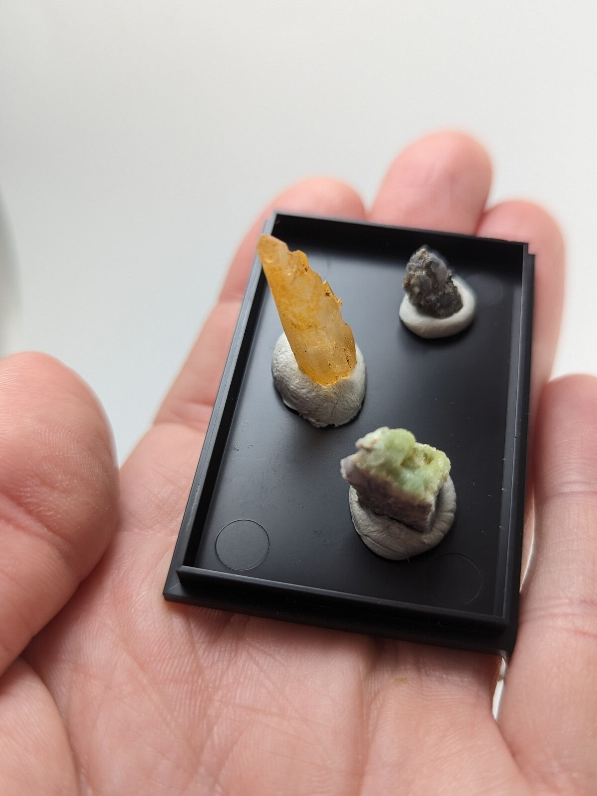 Black rectangular display tray holding three miniature mineral specimens.