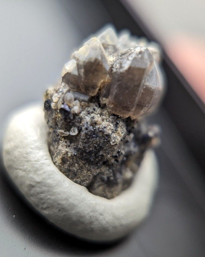 A cluster of translucent brownish crystals with sharp, faceted edges sits atop a smooth white stone base.