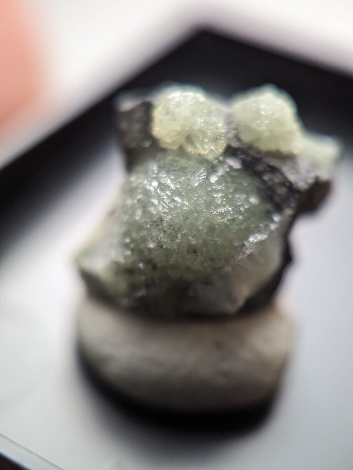 A translucent green crystal formation with a rough, textured surface and two small white crystalline clusters on top.