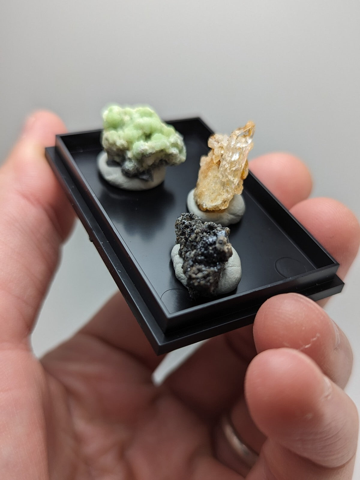 Black rectangular display tray holding three miniature mineral specimens.