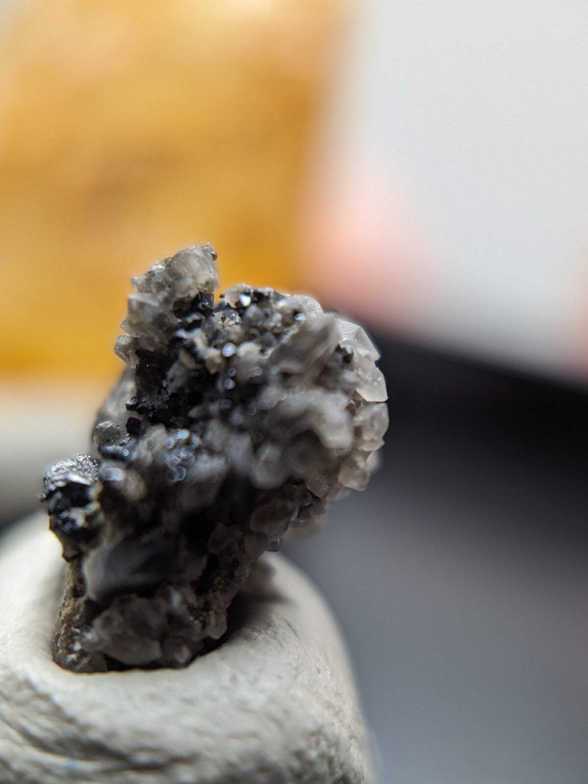 A textured, grayish-black mineral specimen with crystalline formations and dark inclusions.