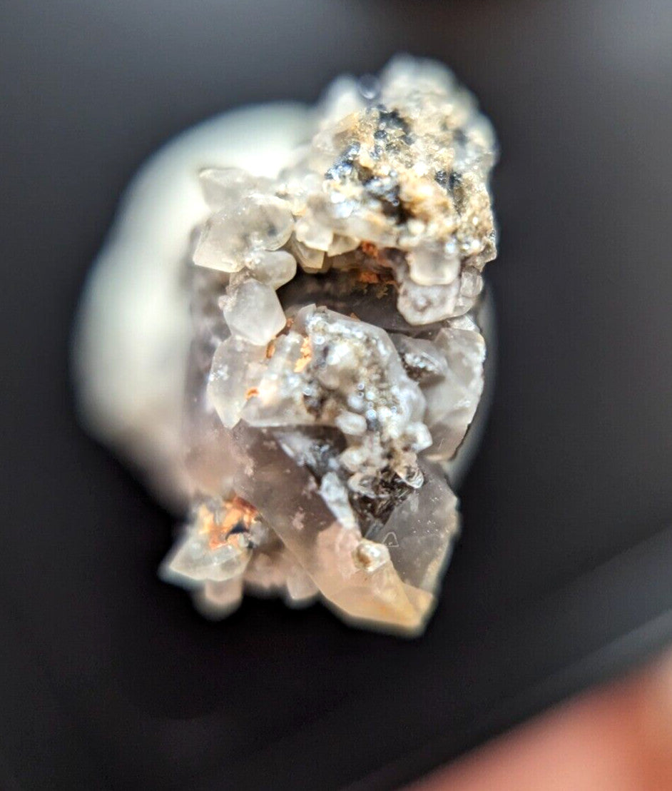 A translucent, crystalline mineral specimen with a mix of clear and milky white quartz crystals intergrown with dark specks and hints of orange.