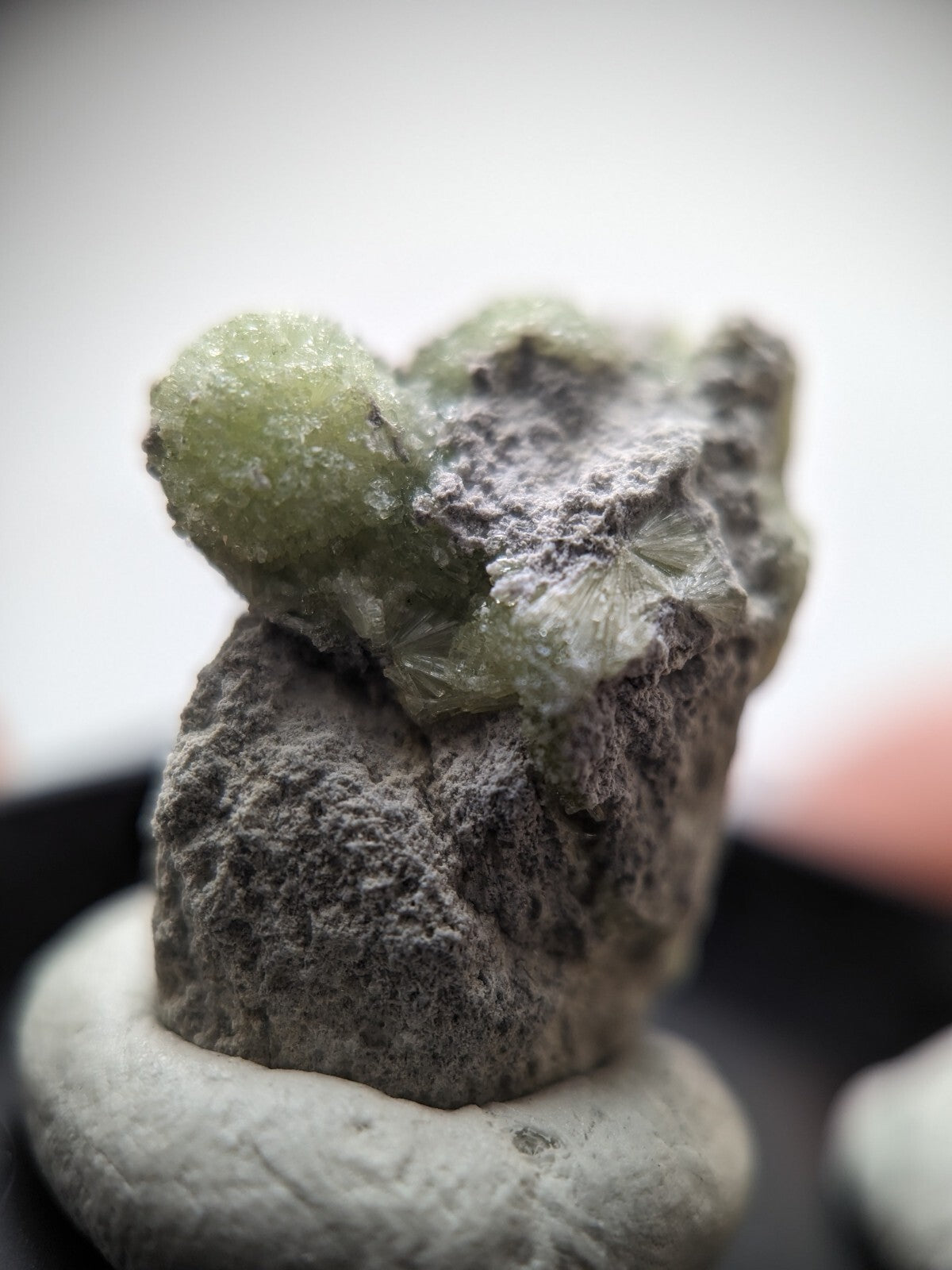 A translucent green mineral specimen with crystalline formations emerging from a rough, grayish rock base.