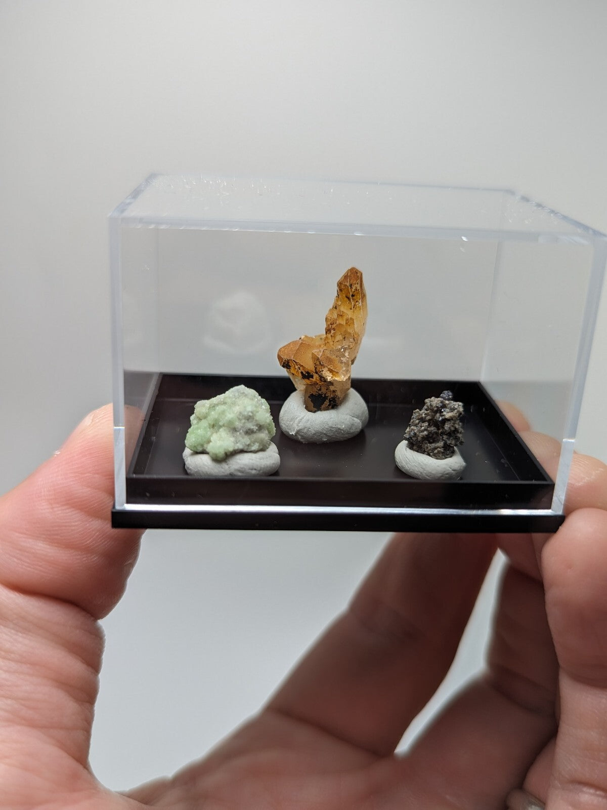 A clear acrylic display case holding three distinct mineral specimens on a black tray.