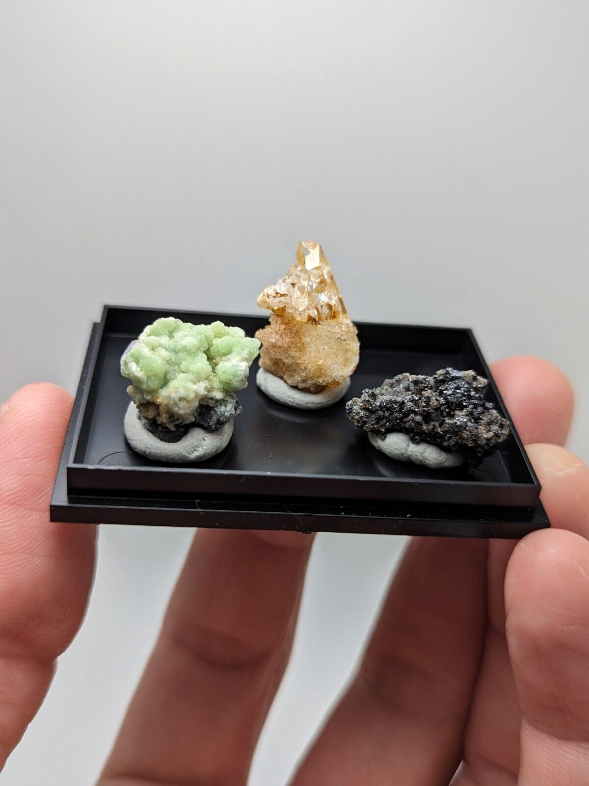 Black rectangular display tray holding three distinct mineral specimens.