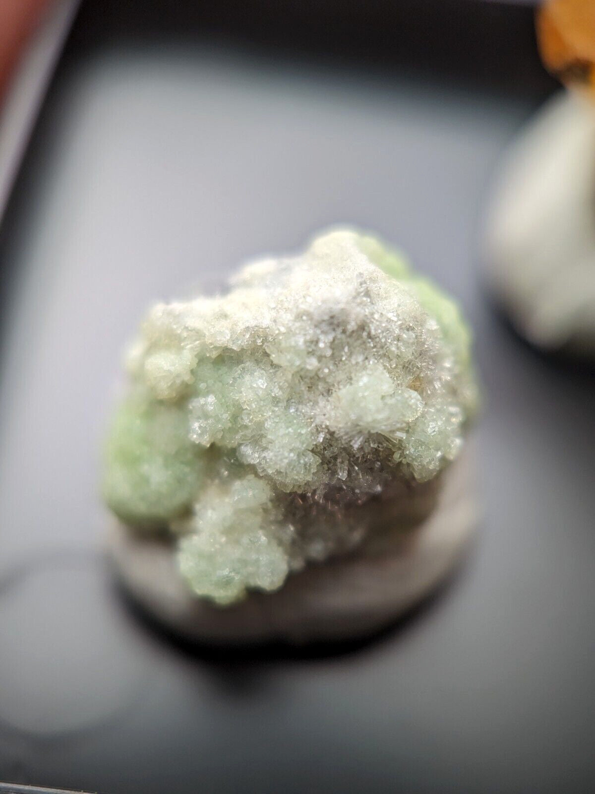 A pale green, crystalline mineral specimen with a textured surface and translucent facets.