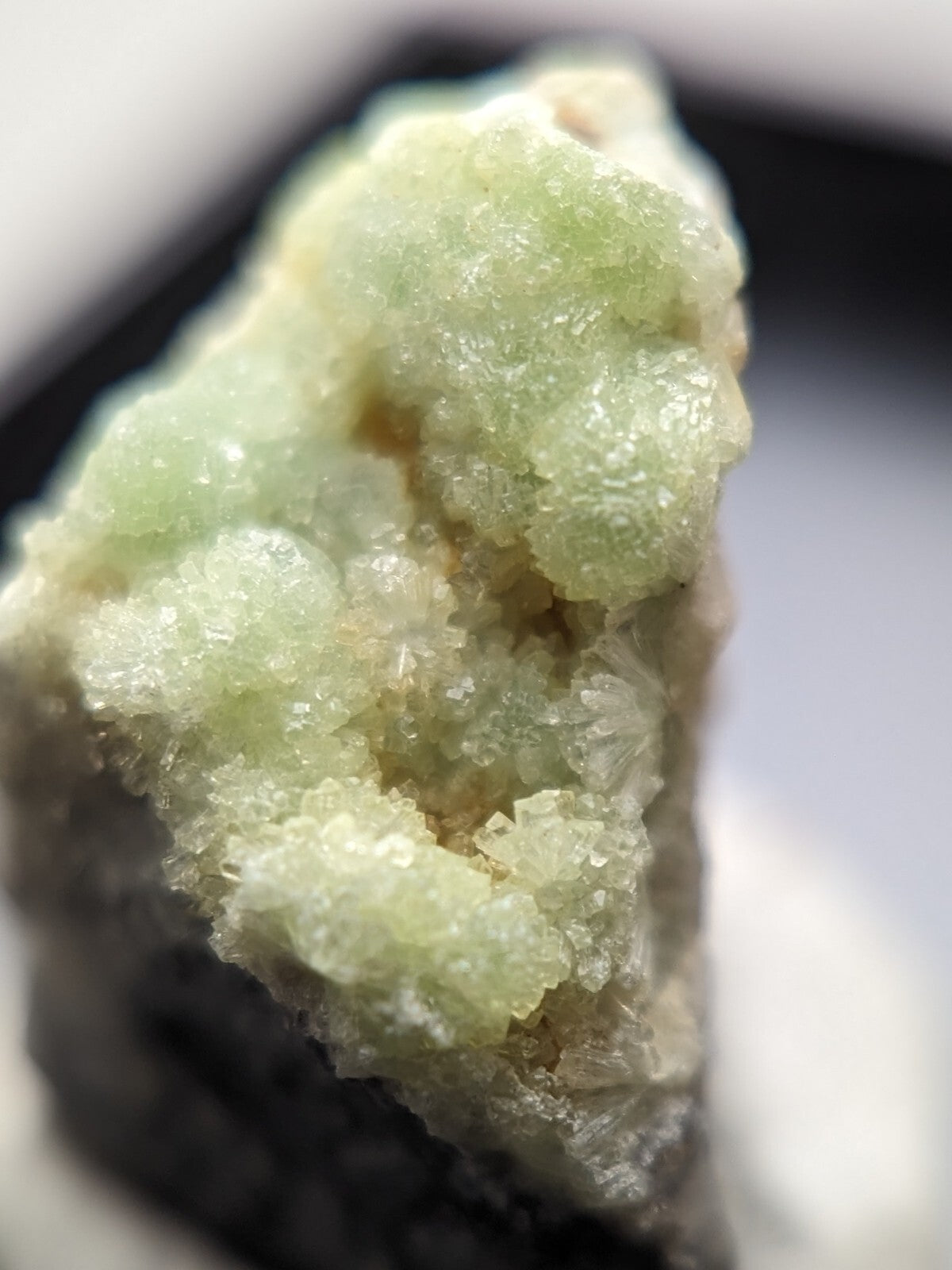 A pale green, crystalline mineral specimen with a rough, textured surface and translucent facets.