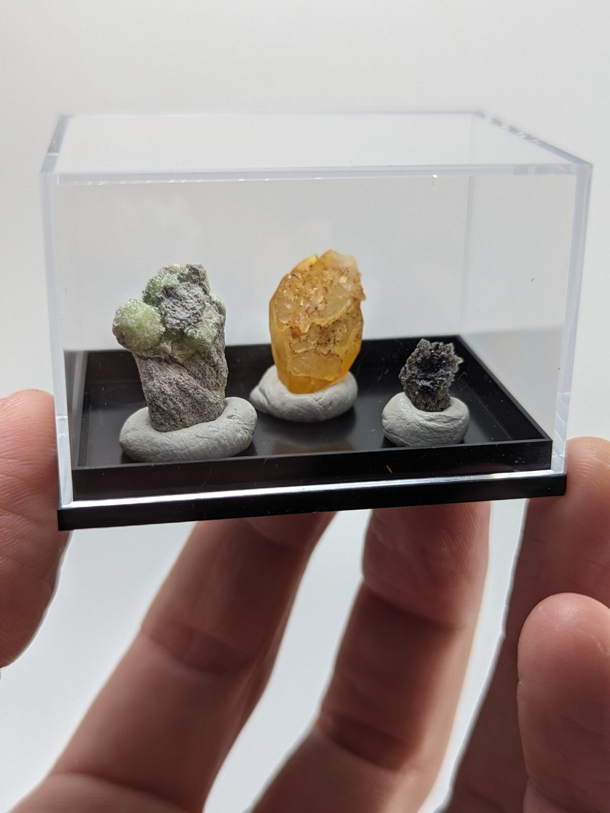 Clear acrylic display case holding three distinct mineral specimens on a black base.