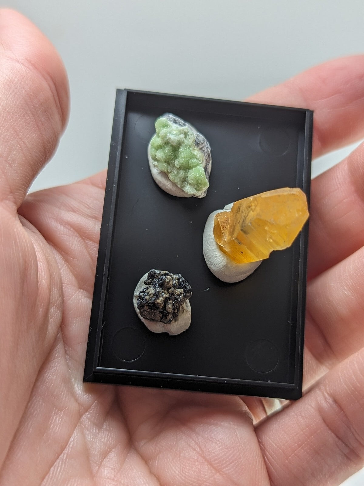 Black rectangular display tray holding three miniature mineral specimens.