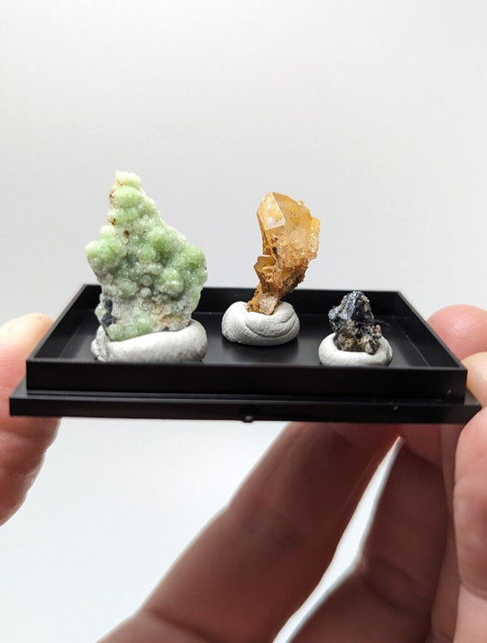 Black rectangular display tray holding three miniature mineral specimens.
