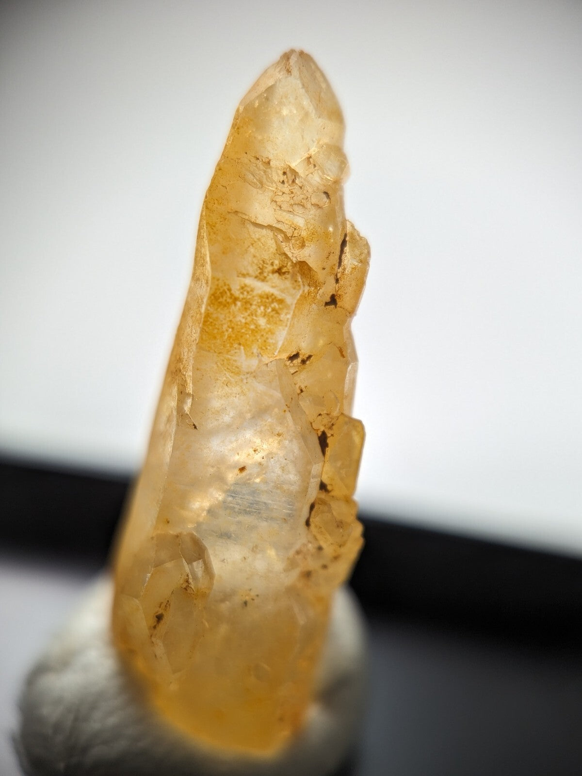 A translucent golden-yellow crystal with a pointed tip and natural facets, displayed on a small stone base.