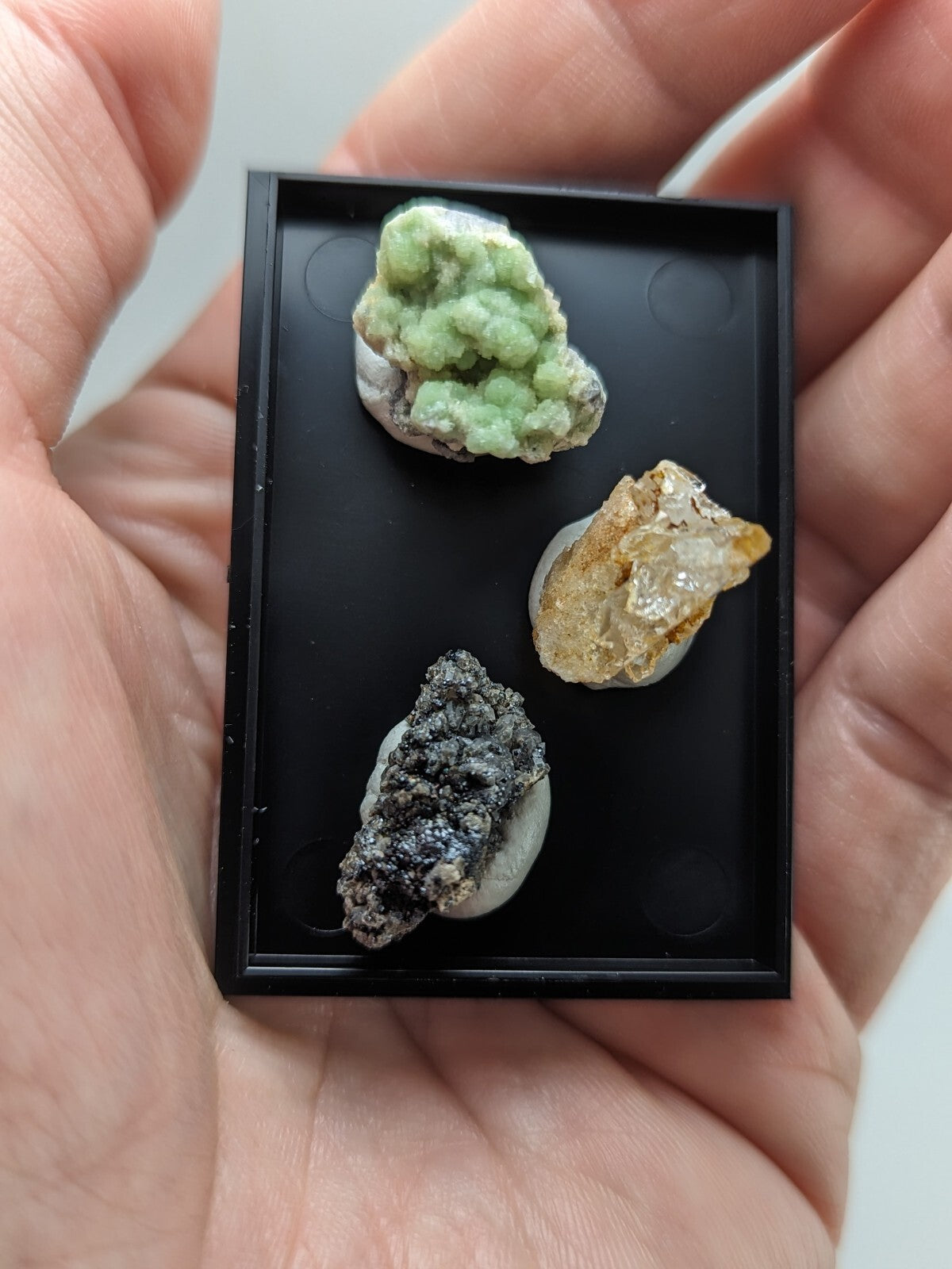 Black rectangular display case holding three distinct mineral specimens.