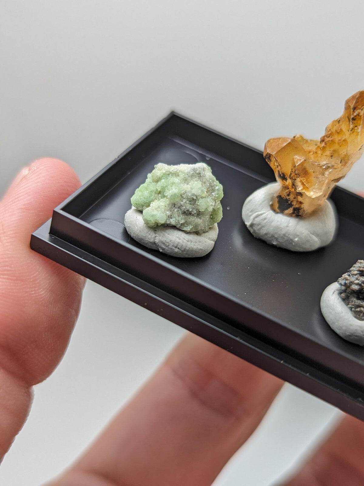 Black rectangular display tray holding three mineral specimens.
