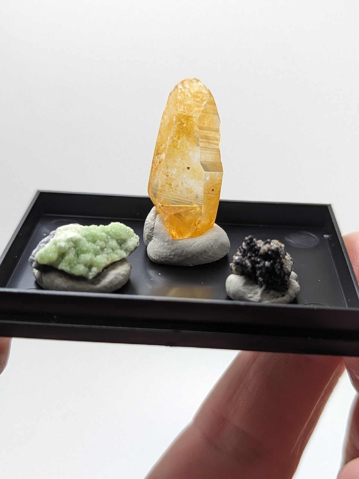 A translucent golden-yellow crystal with visible internal striations, mounted on a gray rock base within a black display tray.