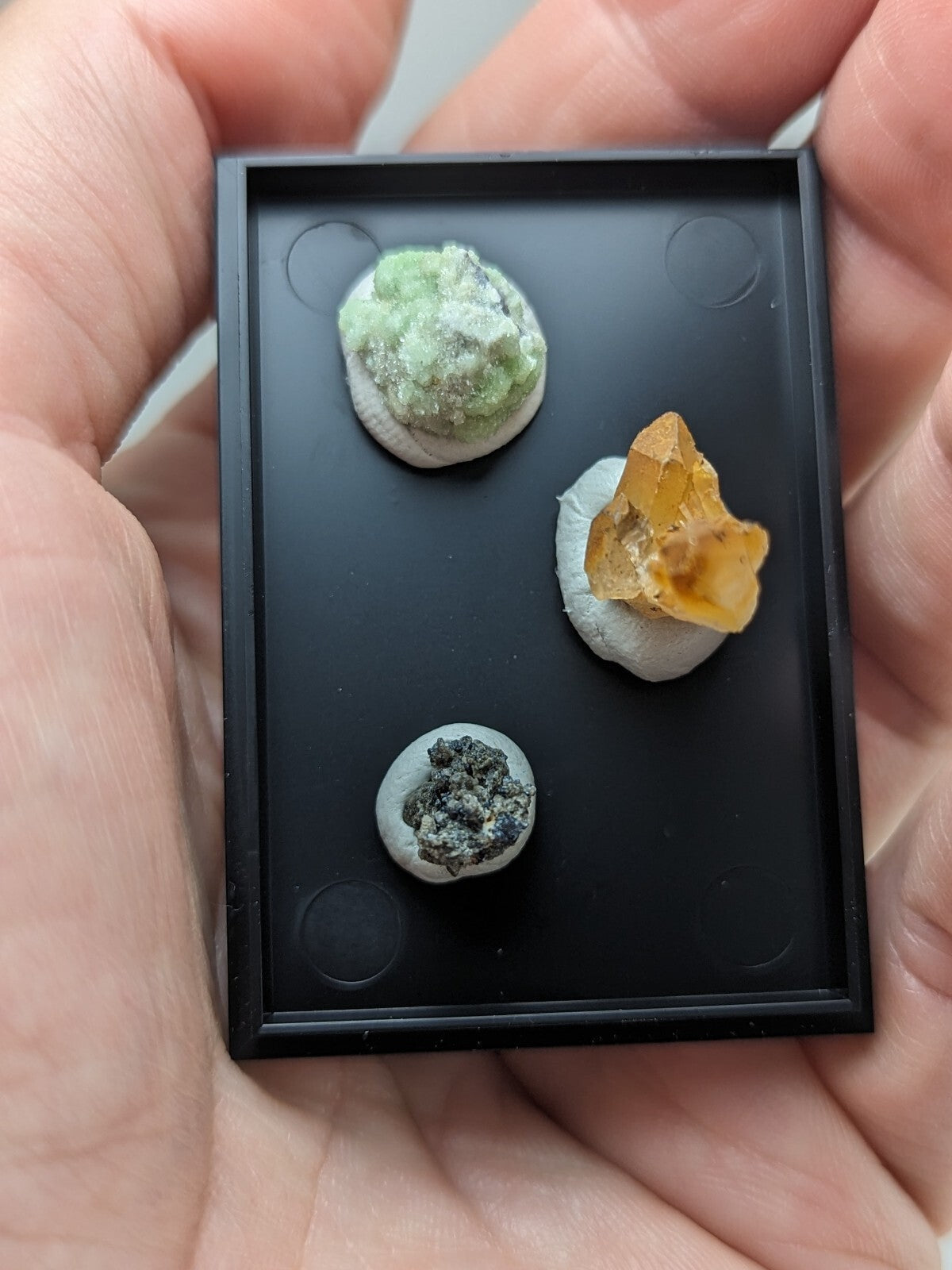 Black rectangular display case holding three miniature mineral specimens.