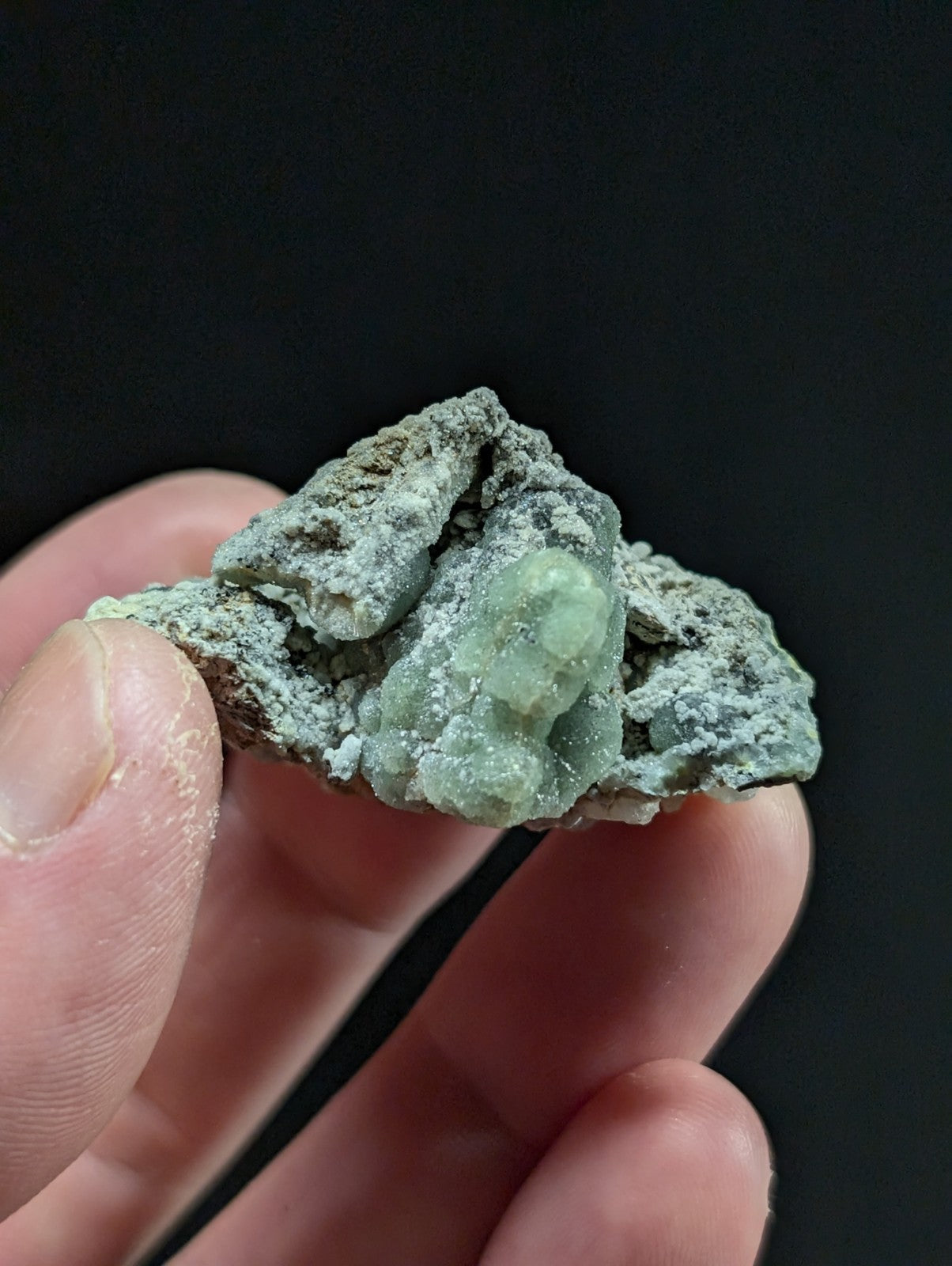 A rough, irregularly shaped mineral specimen with a pale green crystalline formation nestled within a darker, earthy matrix.